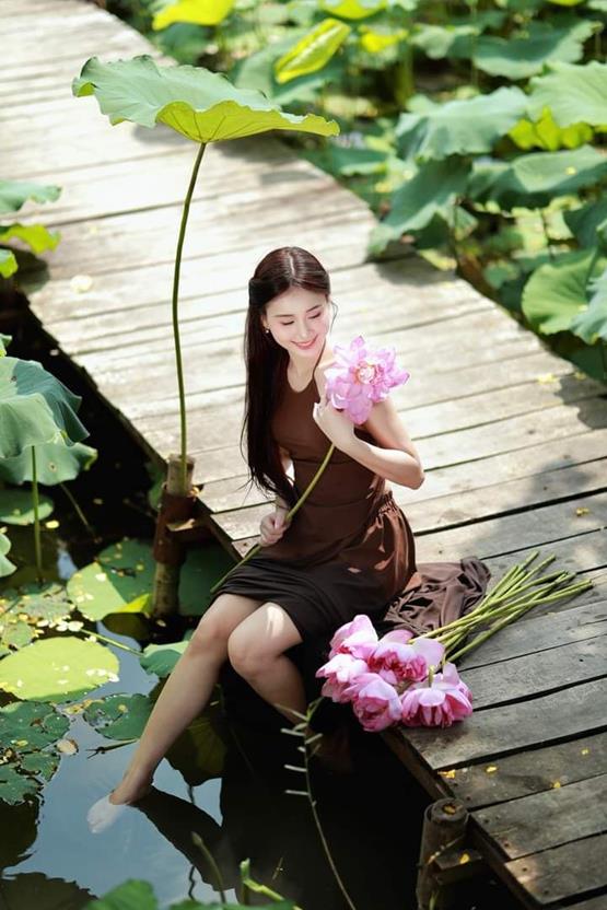 cô gái cầm hoa sen hồng ngồi trên cầu